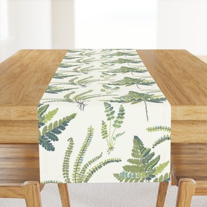 May include: A white table runner with a green fern pattern. The runner is on a wooden table.
