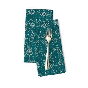 May include: Two teal blue linen napkins with a white geometric pattern. The napkins are folded and a silver fork is placed on top of them.