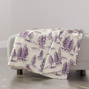 May include: Purple and white throw blanket with a repeating pattern of trees, tents, and a flying saucer. The pattern is reminiscent of a vintage illustration.