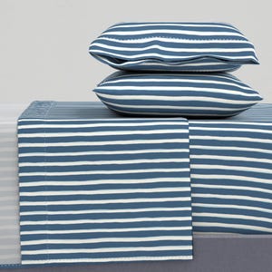 May include: A blue and white striped bedding set. The set includes two pillows and a fitted sheet. The pillows are stacked on top of the fitted sheet. The stripes are horizontal and evenly spaced. The color scheme is a classic nautical theme, reminiscent of seaside decor.