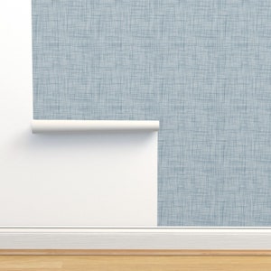 May include: A roll of blue and white patterned wallpaper with a subtle textured finish. The wallpaper is partially unrolled and hanging on a white wall.