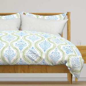 May include: A white duvet cover with a blue and green floral pattern. The duvet cover is on a bed with a wooden headboard.