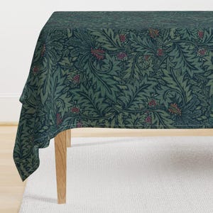 May include: A dark green tablecloth with a floral pattern featuring intricate leaves and small red and pink flowers. The tablecloth is draped over a wooden table with a white surface underneath.