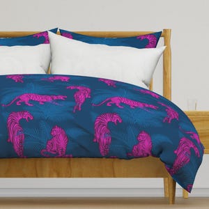 May include: A blue duvet cover featuring a pink tiger print and tropical leaf pattern. The duvet cover is on a bed with a wooden headboard and white pillows.