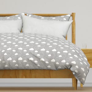 May include: A bed with a wooden frame and a gray duvet cover featuring a white cloud and rain pattern. Two white pillows are visible, along with a matching pillowcase. The bedding set creates a calming, weather-themed aesthetic.