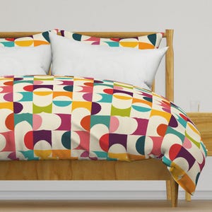 May include: A duvet cover with a geometric pattern featuring colourful circles and squares on a cream background. The duvet cover is on a bed with a wooden headboard and a white pillow.