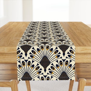 May include: A white table runner with a navy blue and gold peacock design. The runner is on a wooden table.