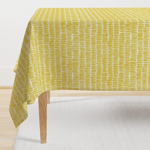May include: A yellow tablecloth with a repeating pattern of small, yellow dashes. The tablecloth is draped over a wooden table.