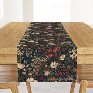 May include: A floral table runner with a dark blue background and a pattern of various flowers in shades of red, cream, and brown. The runner is rectangular and placed on a wooden table.