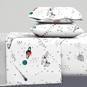 May include: White bedding set with a space-themed print featuring planets, stars, and spaceships. The print is in black and white with accents of red, blue, and green.