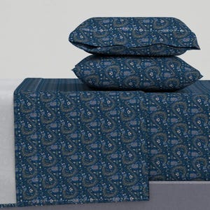 Könnte beinhalten: Ein blaues und goldenes, gemustertes Spannbettlaken und zwei passende Kissenbezüge. Das Laken hat ein florales Design mit kleinen weißen Blüten und goldenen Akzenten.