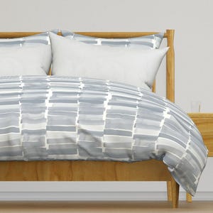May include: A gray and white patterned duvet cover with a subtle watercolor effect. The duvet cover is on a wooden bed frame.