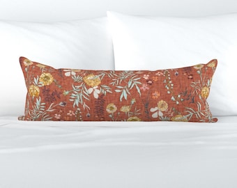 Può includere: Un cuscino lungo e rettangolare con uno sfondo color ruggine e un motivo floreale. I fiori sono in tonalità di rosa, giallo e blu.