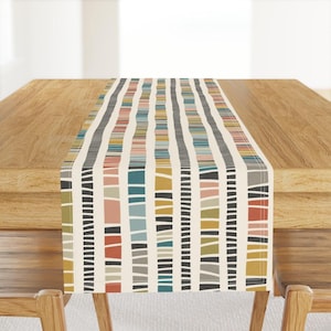 Peut inclure: Chemin de table rectangulaire avec un fond crème et un motif à rayures verticales. Les rayures sont composées de différentes couleurs, dont le noir, le gris, le turquoise, le rose et le jaune. Le chemin de table est posé sur une table en bois.