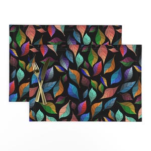 May include: Two black placemats with a colorful leaf pattern. The leaves are outlined in black and filled with various shades of blue, green, red, orange, and yellow.