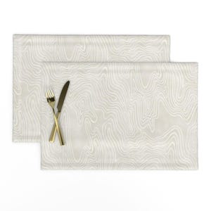 May include: Two rectangular placemats featuring a light beige background with a white wavy, topographic-style line pattern. A gold-toned metal fork and a matching gold-toned metal knife are positioned diagonally across the top placemat.