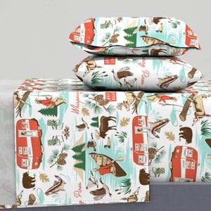 May include: White bedding set with a repeating pattern of red campers, bears, fish, and wildlife. The design includes the text "Whispering Pines" in a cursive font. Two matching pillowcases are stacked on top of the sheet.