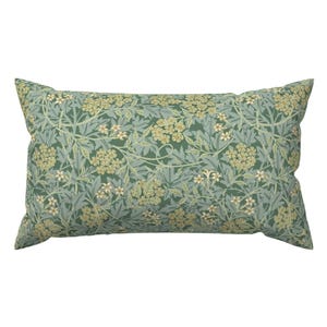May include: A rectangular decorative pillow with a floral pattern. The pillow features a repeating design of green leaves and small, clustered flowers in shades of cream and light green against a teal background. The pillow has a soft, inviting appearance.