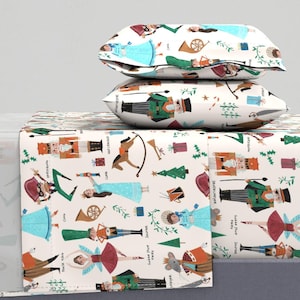 Könnte beinhalten: Ein weißes Bettwäsche-Set mit einem Nussknacker-Motiv. Die Bettwäsche zeigt ein sich wiederholendes Muster aus Nussknacker-Figuren, Weihnachtsbäumen und anderen festlichen Bildern. Das Set beinhaltet ein Spannbettlaken, ein flaches Laken und zwei Kissenbezüge.