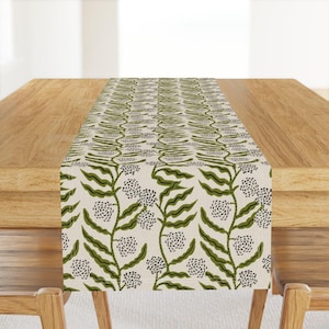 May include: A green and white table runner with a floral pattern. The runner is made of a soft, woven fabric and features a repeating design of green leaves and white flowers.