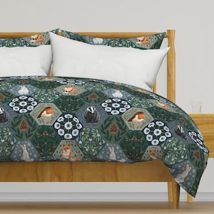 May include: A green, blue, and white duvet cover with a repeating pattern of woodland animals, including foxes, badgers, and robins. The pattern is set against a background of green leaves and white flowers.