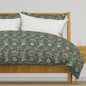 Puede incluir: Una funda nórdica azul verdosa con un patrón floral que presenta un diseño repetitivo de flores y hojas estilizadas. La funda nórdica está sobre un marco de cama de madera con una almohada blanca.