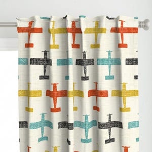 May include: Cream-colored curtain panel featuring a repeating pattern of stylized airplanes in orange, yellow, black, and teal. The planes have a textured, hand-drawn appearance, creating a retro aesthetic. The curtain is hanging on a silver rod.