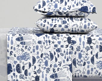 May include: A white and blue bedding set featuring a sea life pattern. The design includes fish, crabs, seahorses, and seaweed. The bedding set comprises a flat sheet, fitted sheet, and two pillowcases.