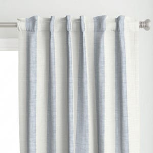 May include: A pair of light blue and white striped curtains hanging from a silver rod. The curtains have vertical stripes, alternating between a light blue and white color. The fabric appears to be a linen or cotton blend.