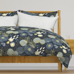 Puede incluir: Una funda nórdica azul marino con un patrón floral blanco y dorado. La funda nórdica está sobre un marco de cama de madera.