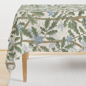 May include: A rectangular tablecloth featuring a repeating pattern of green oak leaves, light blue flowers, and brown branches on a cream background. The tablecloth is draped over a wooden table, creating a decorative and nature-inspired aesthetic.