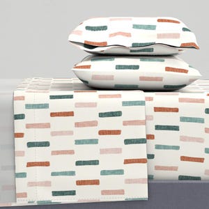 May include: Cream-coloured bedding set with a repeating pattern of teal, coral, and pink horizontal brushstrokes. The set includes two pillowcases and a fitted sheet. The pillowcases are stacked on top of the fitted sheet.