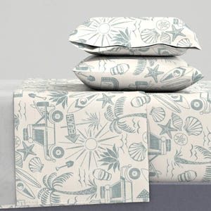 May include: A bedding set featuring two stacked pillows and a flat sheet with a repeating pattern in muted blue on a cream background. The print includes illustrations of palm trees, suns, starfish, seashells, surfboards, and beach vehicles.