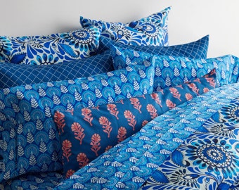 May include: A stack of blue and white patterned throw pillows with a floral design. The pillows are arranged on a bed with a blue and white patterned duvet cover.