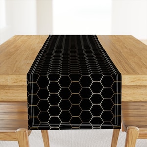 Könnte beinhalten: Schwarzer und goldener geometrischer Tischläufer mit einem Wabenmuster. Der Läufer liegt auf einem Holztisch.