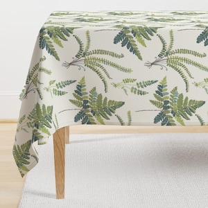 May include: A white tablecloth with a repeating pattern of green ferns. The tablecloth is draped over a table with wooden legs.
