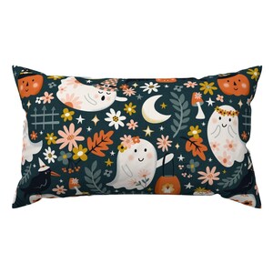 May include: A teal blue pillow with a repeating pattern of ghosts, flowers, and pumpkins. The ghosts are white with black eyes and smiles, and they are wearing floral crowns. The flowers are pink, orange, and yellow. The pumpkins are orange with black eyes and smiles.