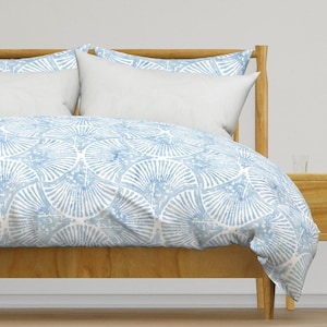 May include: A blue and white patterned duvet cover with a geometric design. The duvet cover is on a bed with a wooden headboard and a white pillow.