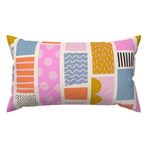 Peut inclure: Un oreiller rectangulaire avec un motif géométrique en rose, bleu, jaune, orange et blanc. Le motif est composé de différentes formes, notamment des cercles, des rayures et des vagues.