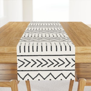 May include: A white table runner with a black geometric pattern. The pattern features a variety of shapes, including diamonds, triangles, and zigzags.