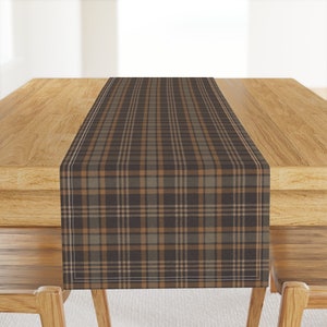 May include: A brown and tan plaid table runner with a white border. The runner is on a wooden table.