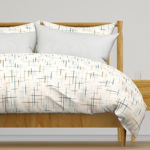 May include: A duvet cover and matching pillow shams featuring an off-white base with a repeating pattern of thin, intersecting horizontal and vertical lines in shades of muted blue, teal, and burnt orange, draped over a wooden bed frame.