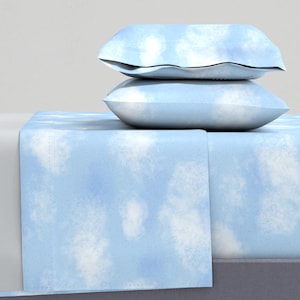 May include: A set of bedding featuring two rectangular pillows stacked on top of a flat sheet. The fabric is light blue with a white, cloud-like mottled pattern throughout. The pillows are plump and the sheet is draped over a rectangular base.