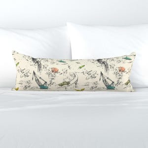 Puede incluir: Una almohada corporal de color crema con un patrón caprichoso que presenta aviones, coches, grúas y animales. El diseño incluye acentos verdes, marrones y azules. La almohada es rectangular y descansa sobre una superficie blanca.