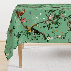 May include: A tablecloth featuring a light green background with a repeating pattern of brown and black monkeys climbing on dark brown tree branches, interspersed with white flowers, small colorful butterflies, and various green leaves.