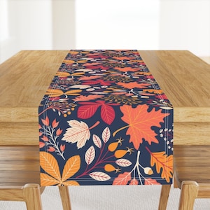 May include: A table runner with a fall-themed design featuring orange, red, and yellow leaves on a dark blue background.