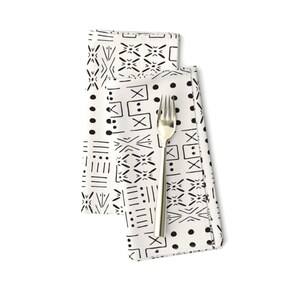 May include: Two white cloth napkins with a black and white geometric pattern. The napkins are folded and a silver fork is placed on top of them.