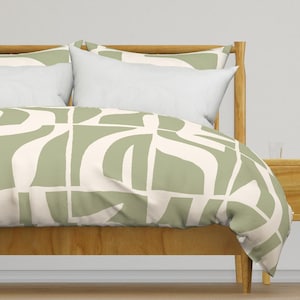 May include: A sage green and white duvet cover with an abstract geometric pattern. The duvet cover is on a wooden bed frame with a white headboard.