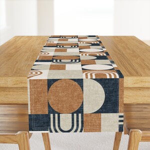 May include: A geometric table runner with a navy blue, brown, white, and beige pattern. The runner features circles, squares, and arches.