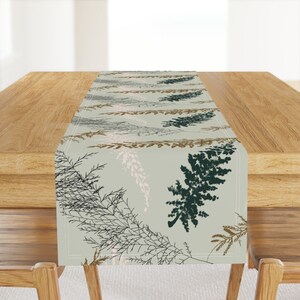 May include: A light green table runner with a repeating pattern of brown, black, and green stylized leaves.